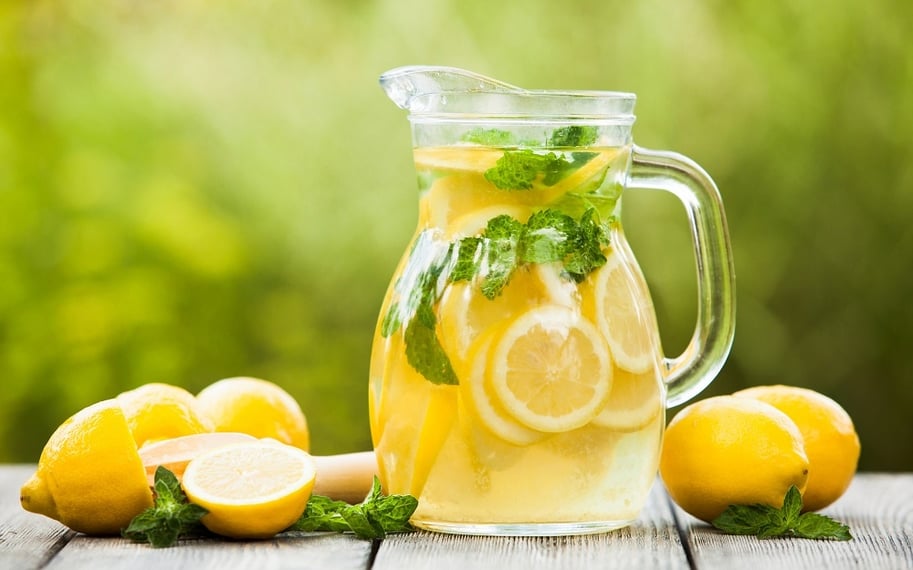 A jug of lemonade with lemons surround it on the table